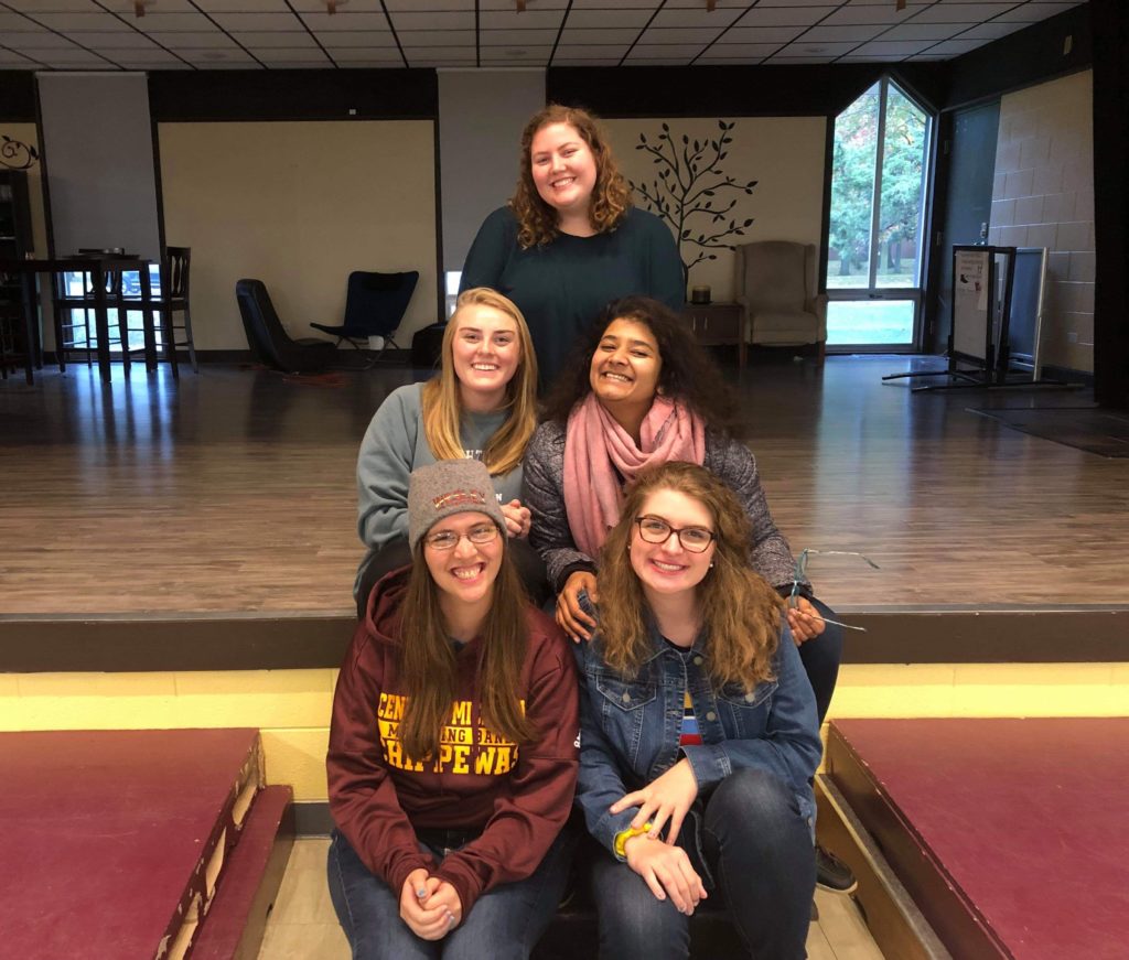Five students smiling and sitting on the Wesley at CMU stage.